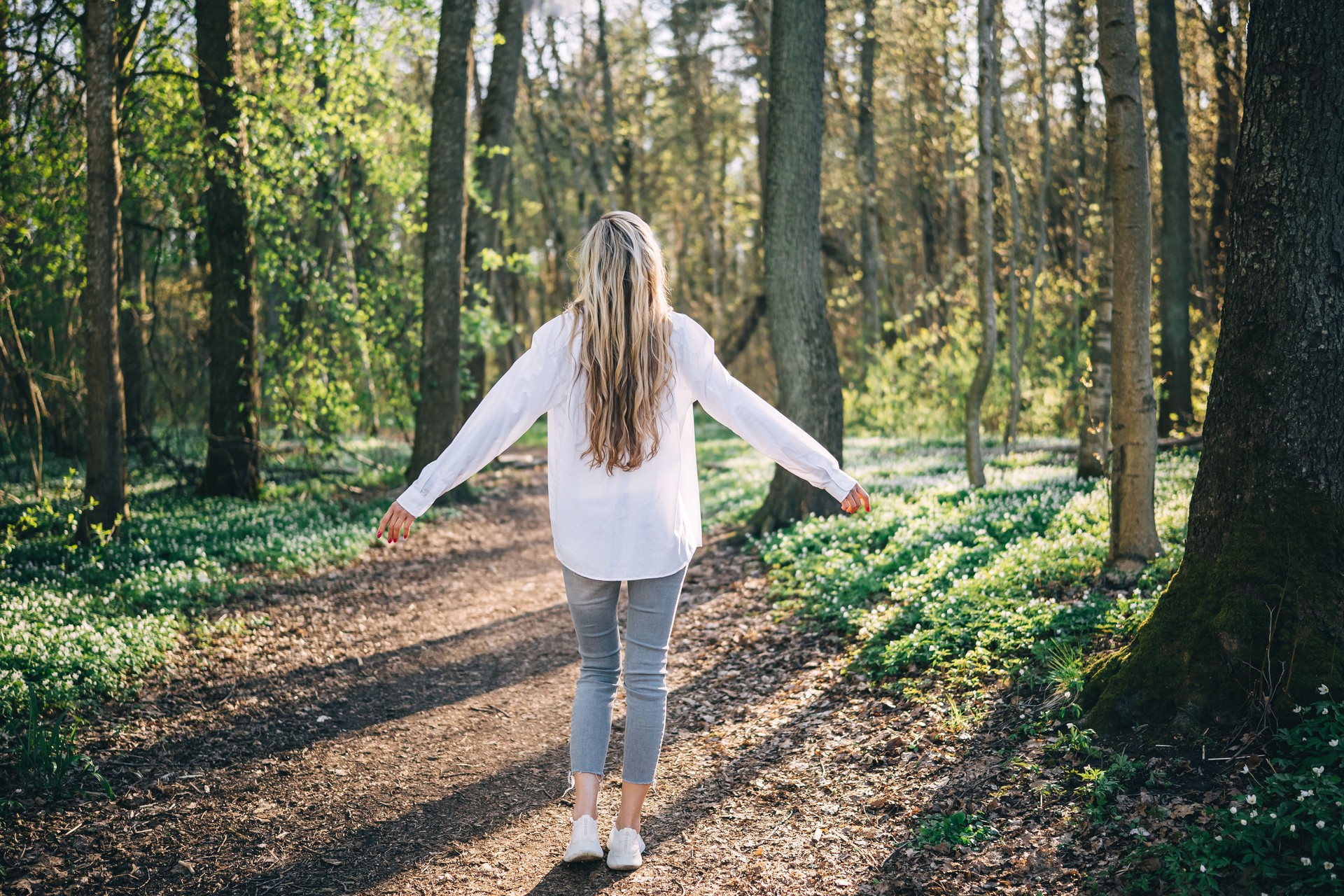 Rear view of young woman arms raised enjoying fresh air in spring forest.